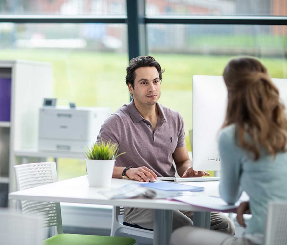 Male sat at a desk talking to a woman
